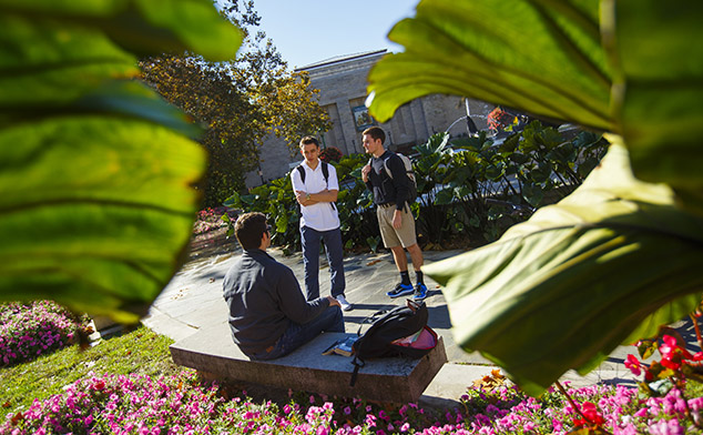 Peek-a-boo style photo of three male students talking with the IU Auditorium in the background.
