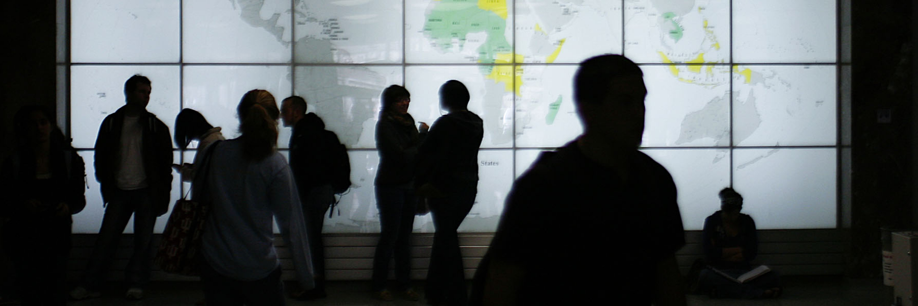 A group of students in shadow in front of a world map.